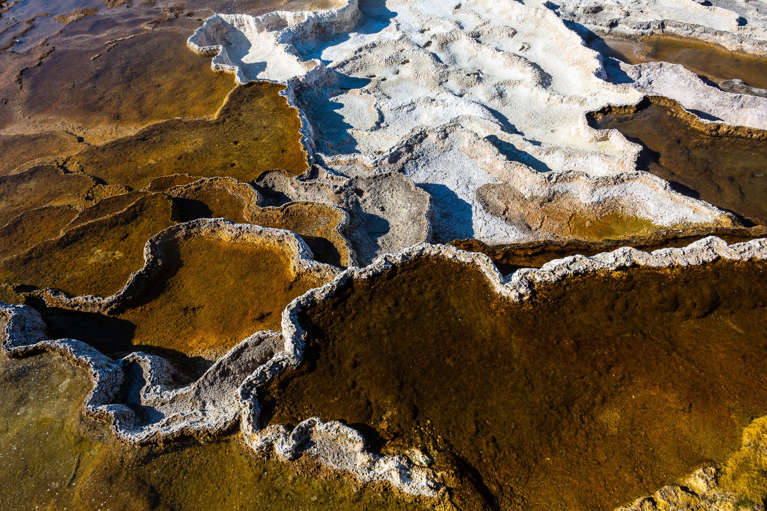 Close-up aerial view of salt flats and mineral deposits with white and brown textured formations and patches of water.