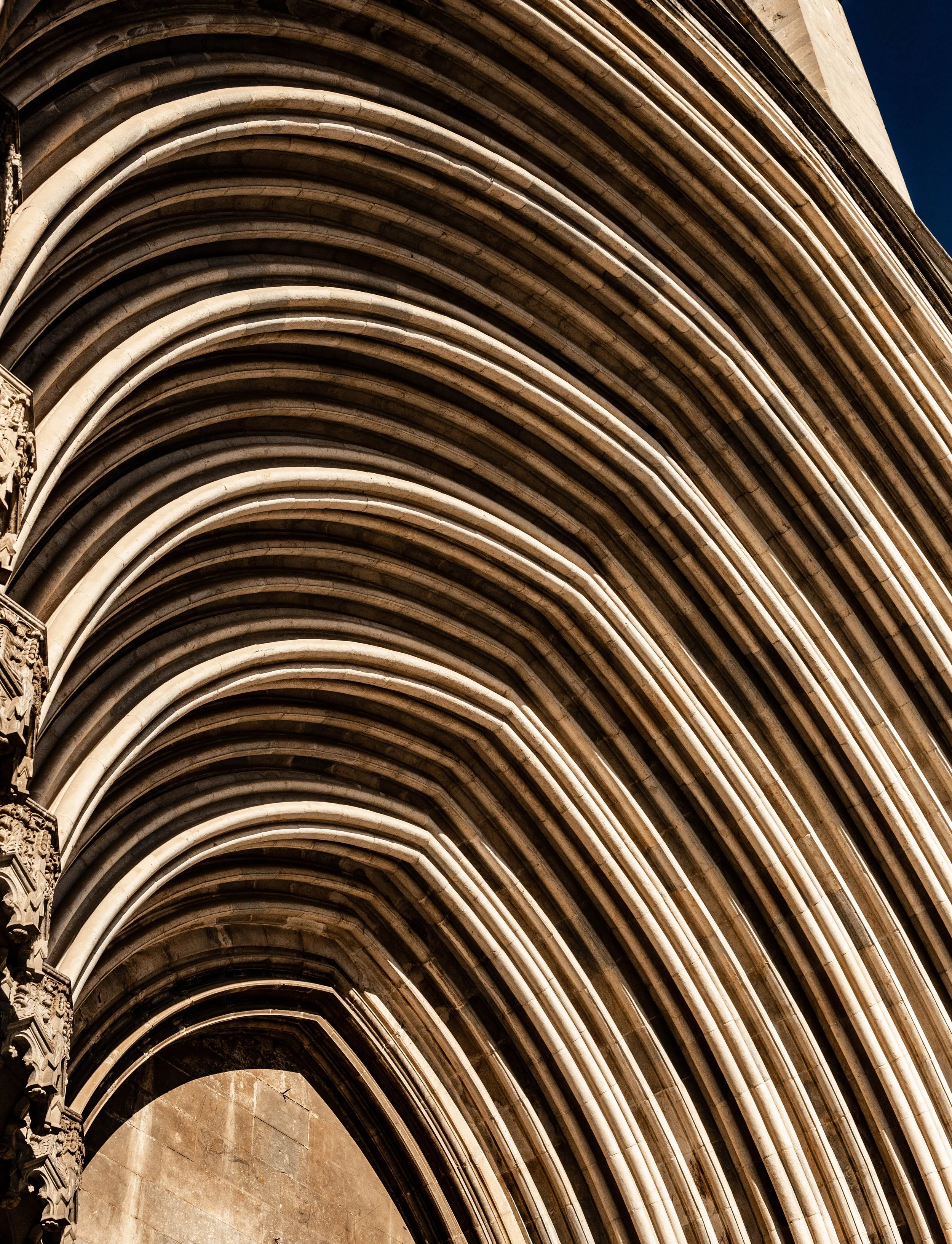 Close-up view of Gothic architectural arches made of stone on a building, with intricate carvings and a deep blue sky in the background.