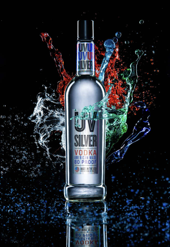 A silver bottle of UV Silver vodka with colorful splashes of water around it, set against a black background.
