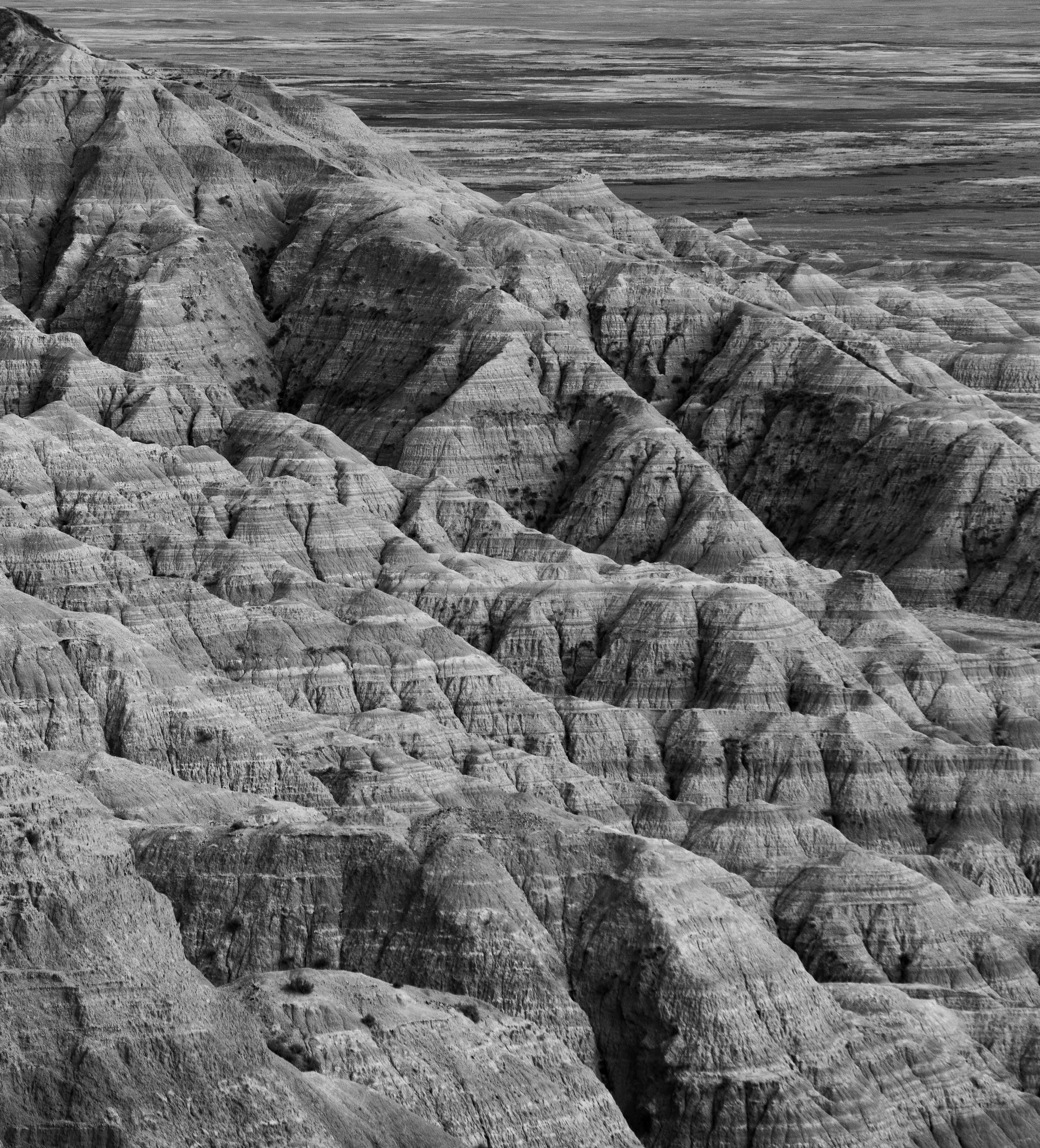 Black and white photograph of rugged mountain landscape with layered rock formations and sparse vegetation.