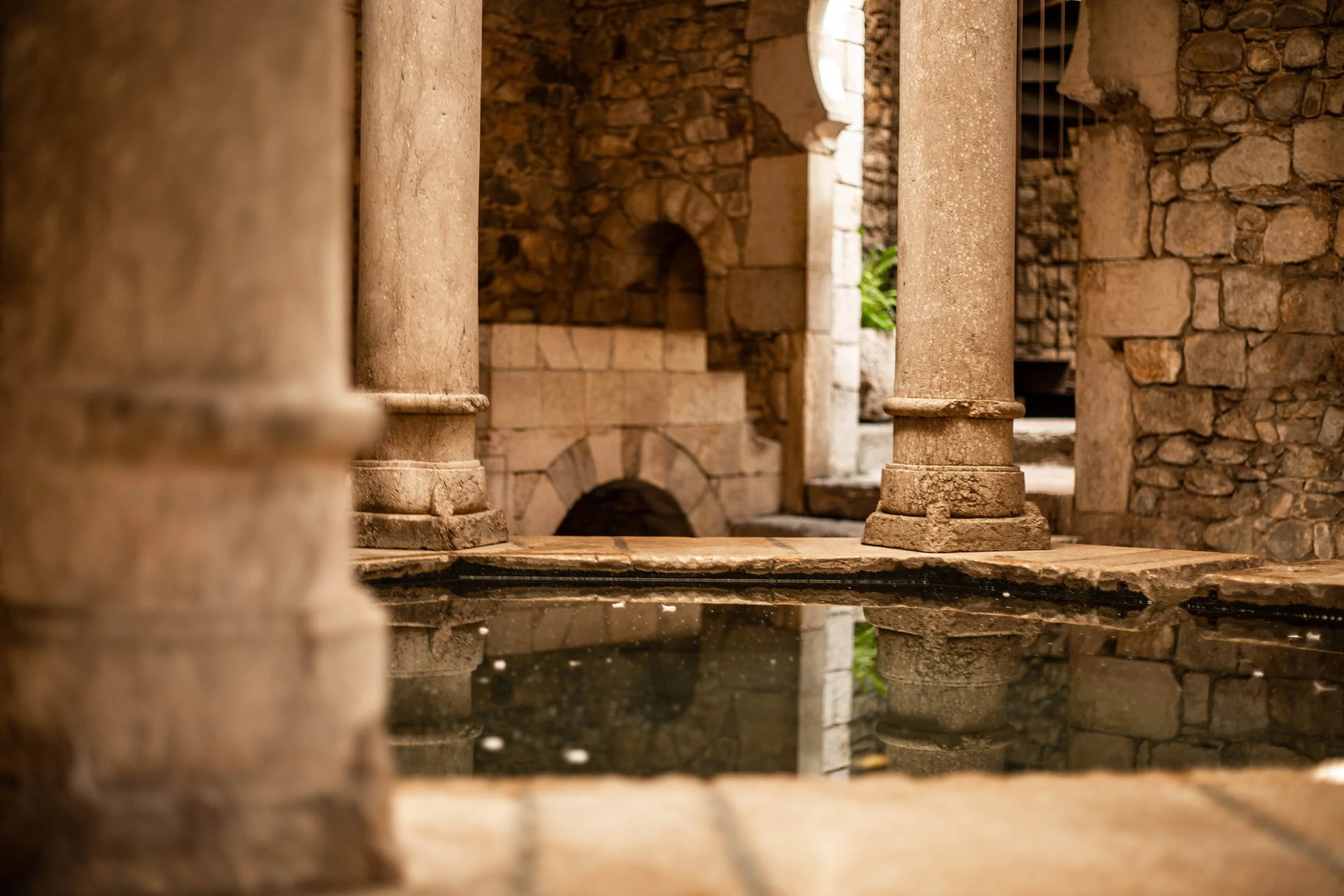 Ancient stone pillars and walls with a small fountain or pool in front, capturing a historical or archaeological setting.