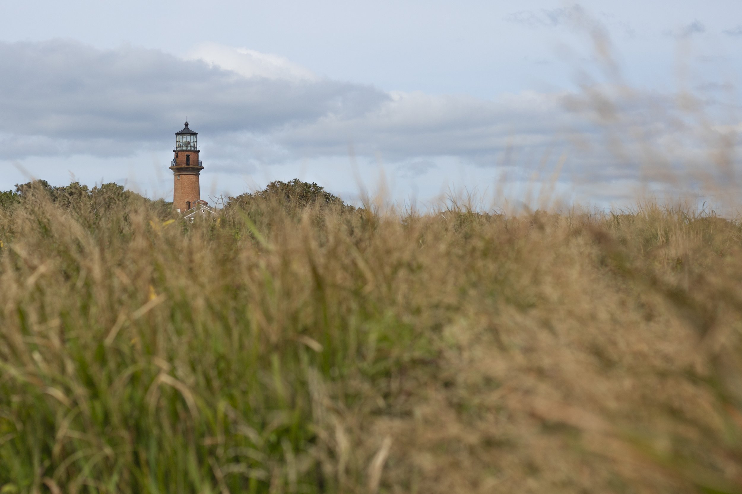 A lighthouse on a grassy landscape with cloudy sky in the background.