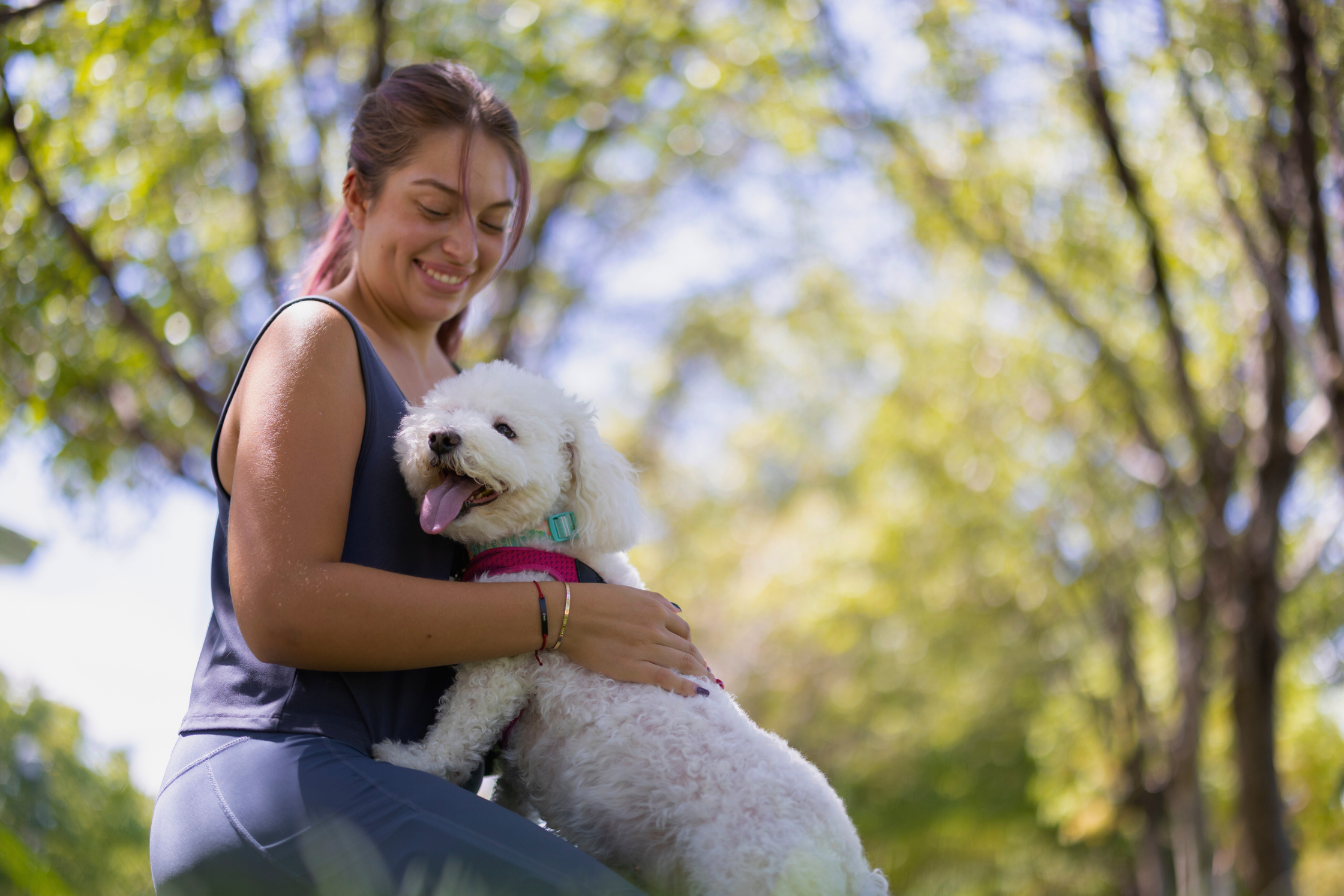 A woman is in a park sitting with her dog, smiling and displaying the care needed for a dog or pet who needs an MRI.