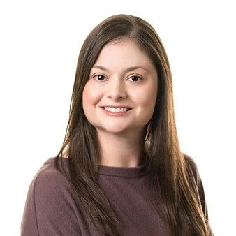 A young woman with long brown hair smiling at the camera against a white background.