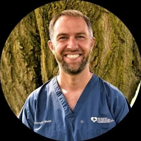 A man smiling in a blue medical uniform with the name tag 'Christen Weder' standing outdoors in front of a tree.