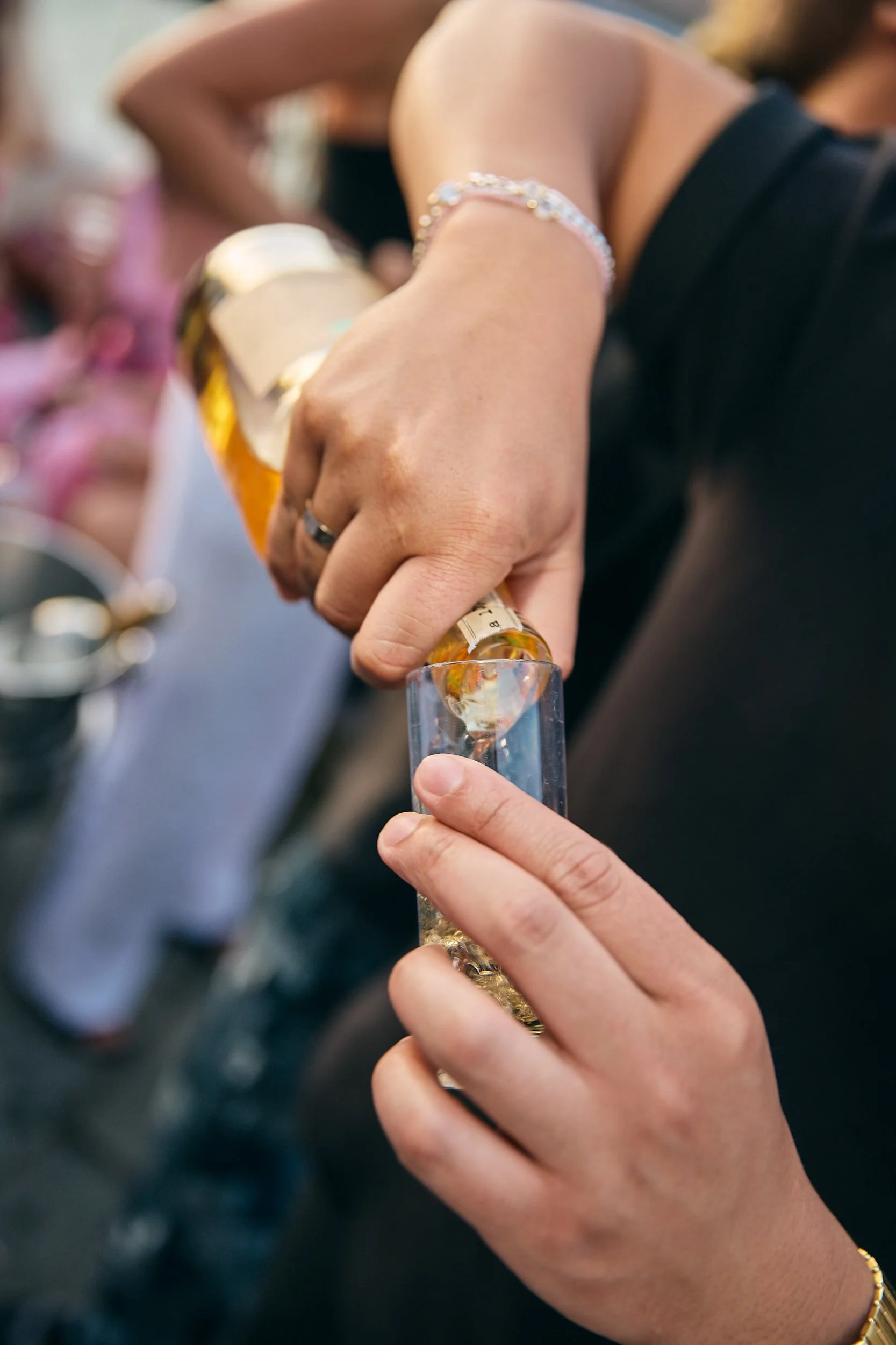 A person pouring a drink from a bottle into a shot glass at a social gathering.