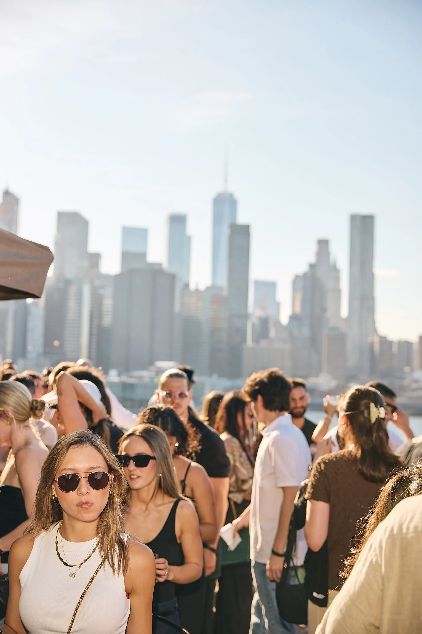 Group of people outdoors with a city skyline in the background, some wearing sunglasses and summer clothing.