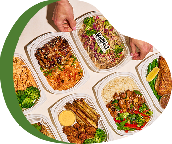 A person reaching for a plastic food container with salad, surrounded by other containers with fried chicken, rice, and vegetables on a white surface.