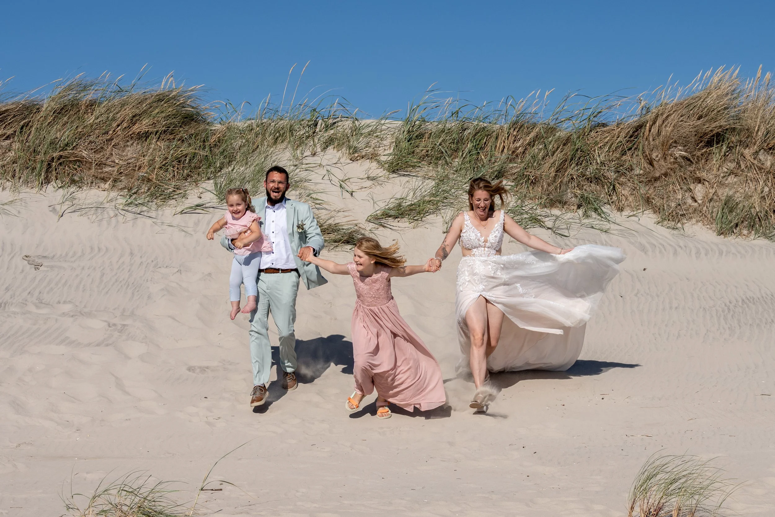 a family running down the dunes, holding hands, laughing