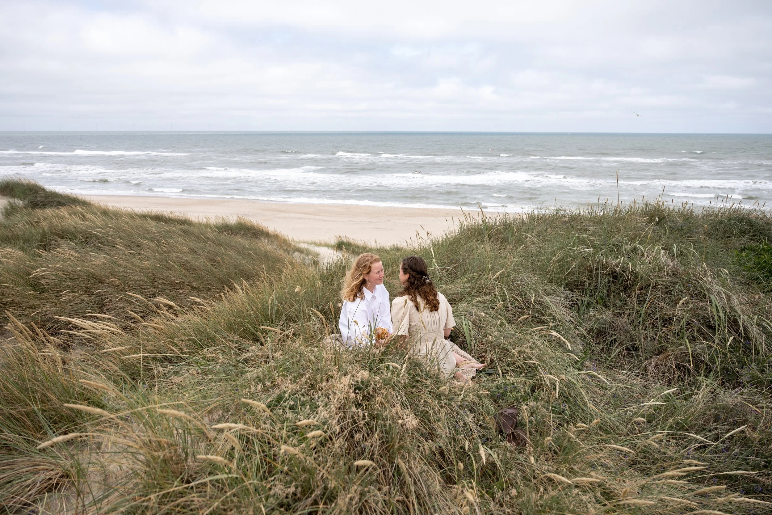 two women sitting in the dunes having a quiet moment with the ocean in the background
