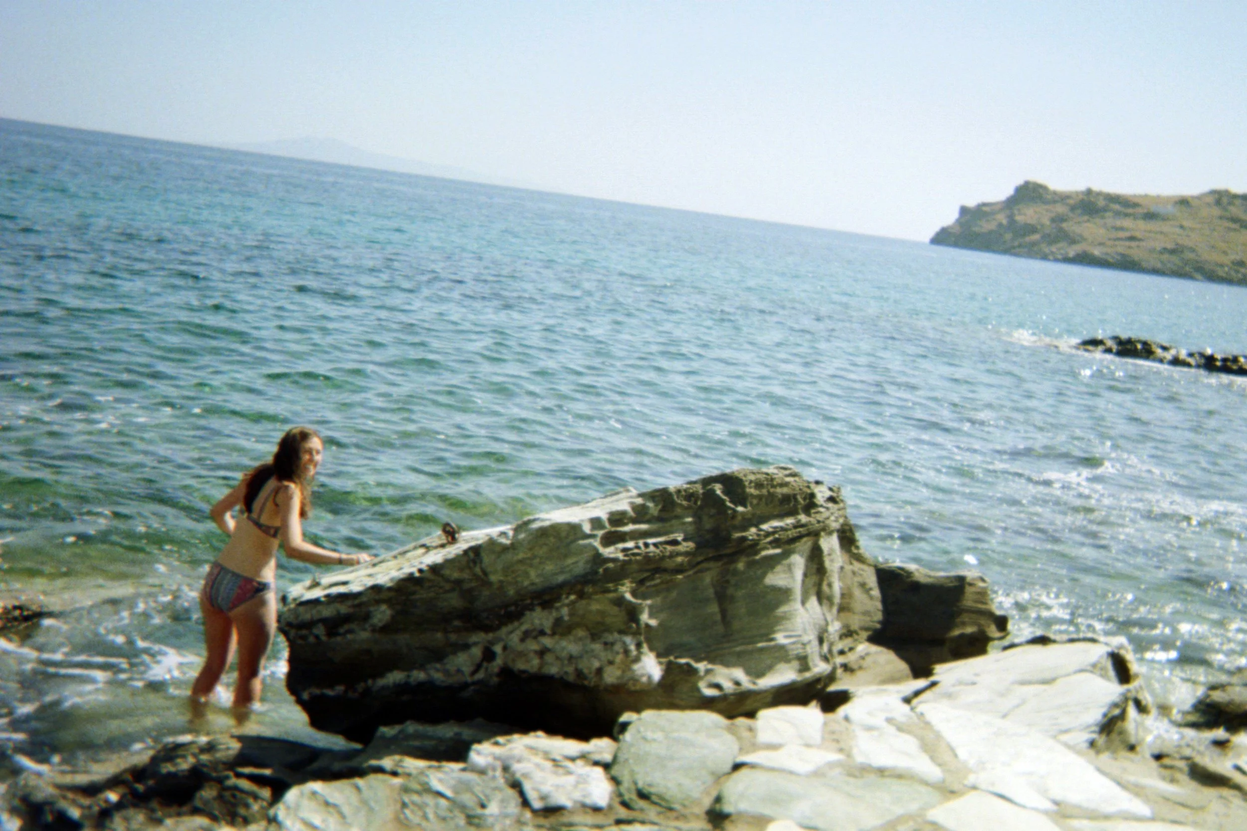 Person in swimsuit climbing rocky shore near the sea under a clear sky.