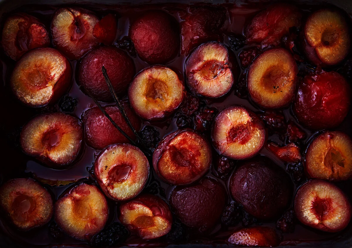 A tray bake of roast plums in their own juices surrounded by vanilla and blackberries. The baked fruit were shot as part of a breakfast brunch series based around homemade granola shot by food photographer and tabletop director Scott Grummett