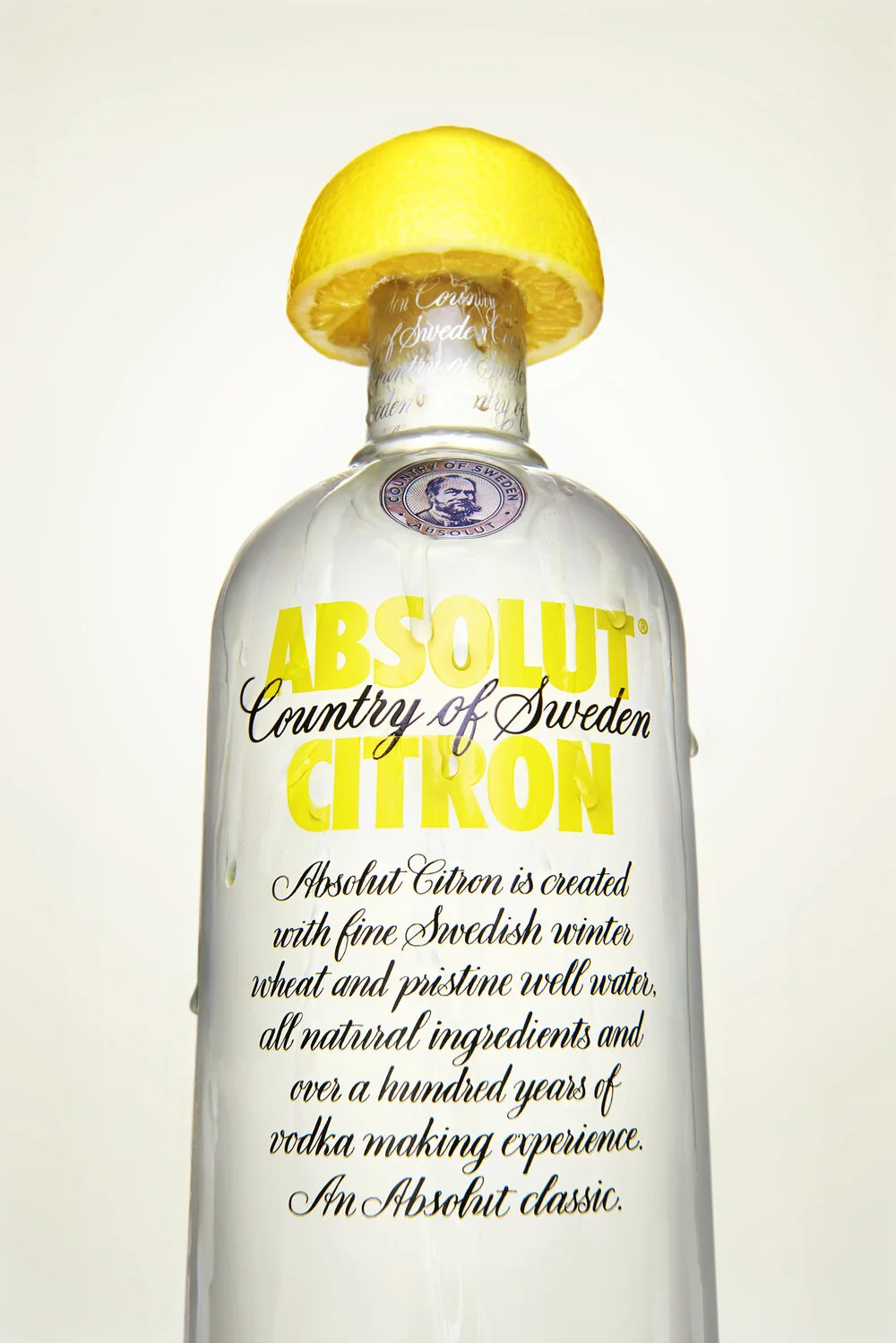 Absolute citron advertising shot of lemon vodka. The lemon squeezing over the top of the bottle.