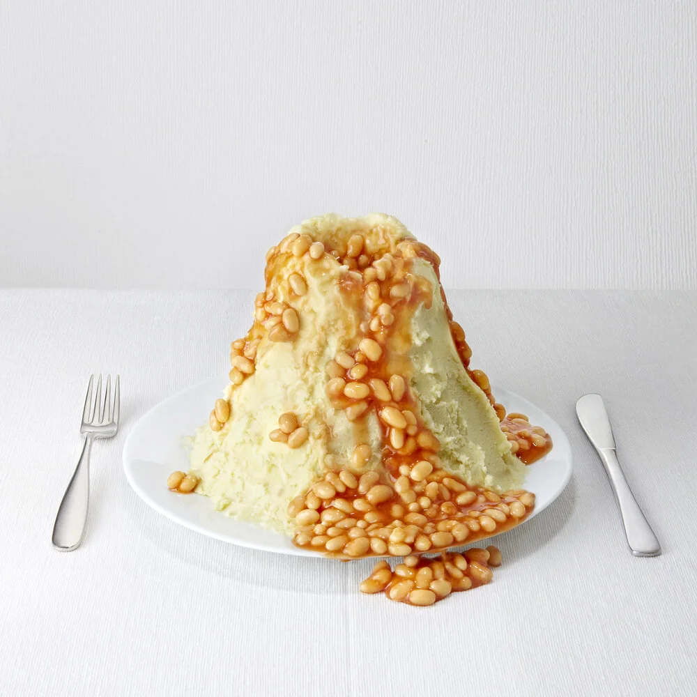 Graphic photograph of food shot in an advertising style. Baked beans piled high in a volcano made of mash potato courtesy of food photographer Scott Grummett based in London.