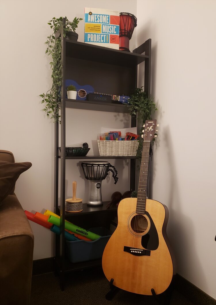 Black metal shelving unit with music items, including a guitar, djembe, ukulele, and music books, decorated with small plants and a wicker basket with colorful markers.