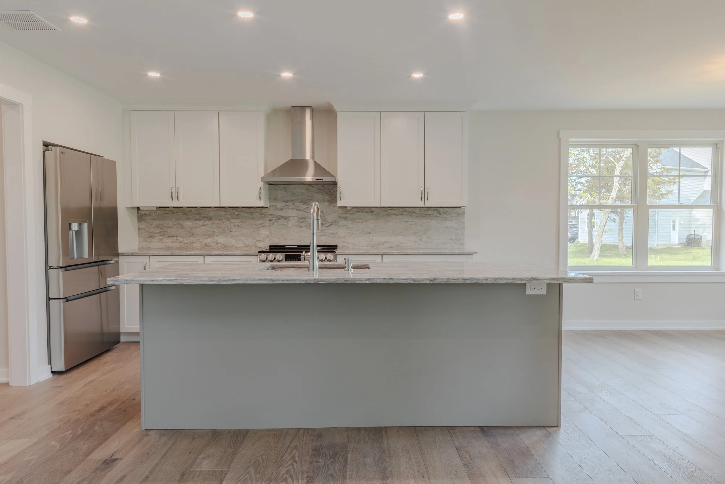 Modern kitchen with white cabinets, marble backsplash, stainless steel refrigerator, large window, and a kitchen island with a gray base and marble countertop.