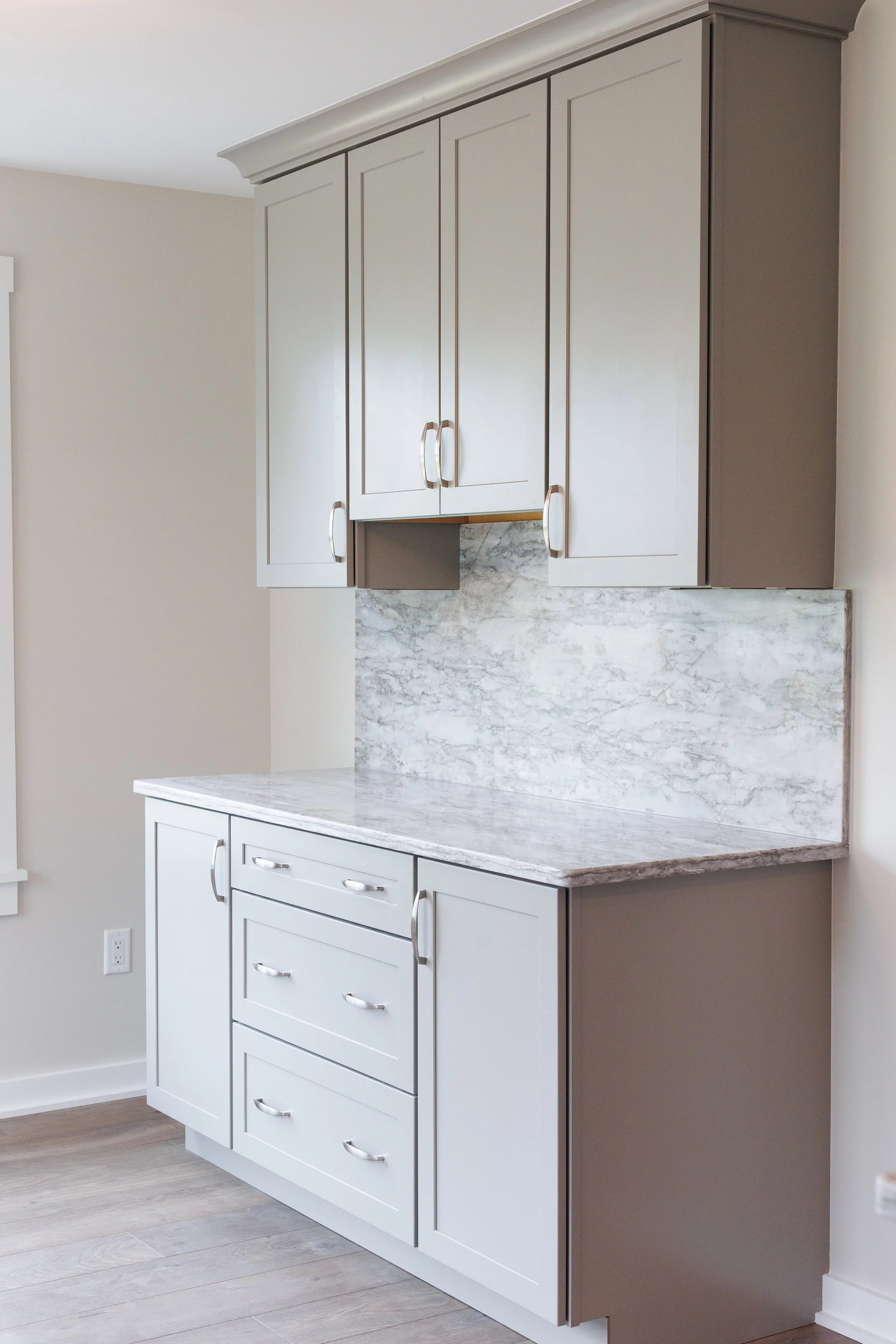 White kitchen cabinet with drawers and doors, marble countertop, and beige walls.