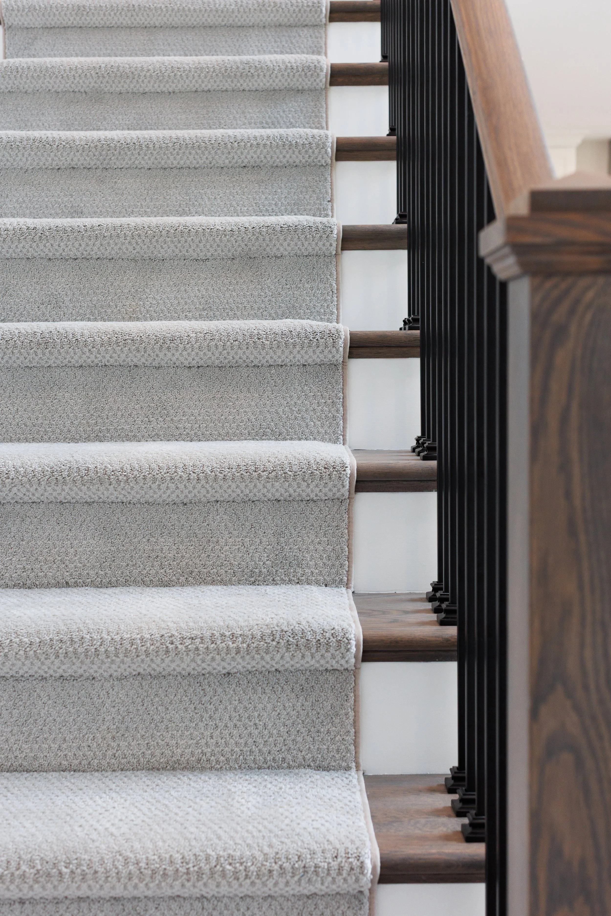 View of a carpeted staircase with white textured carpeting, wooden steps, and black metal balusters with a wooden handrail on the right side.