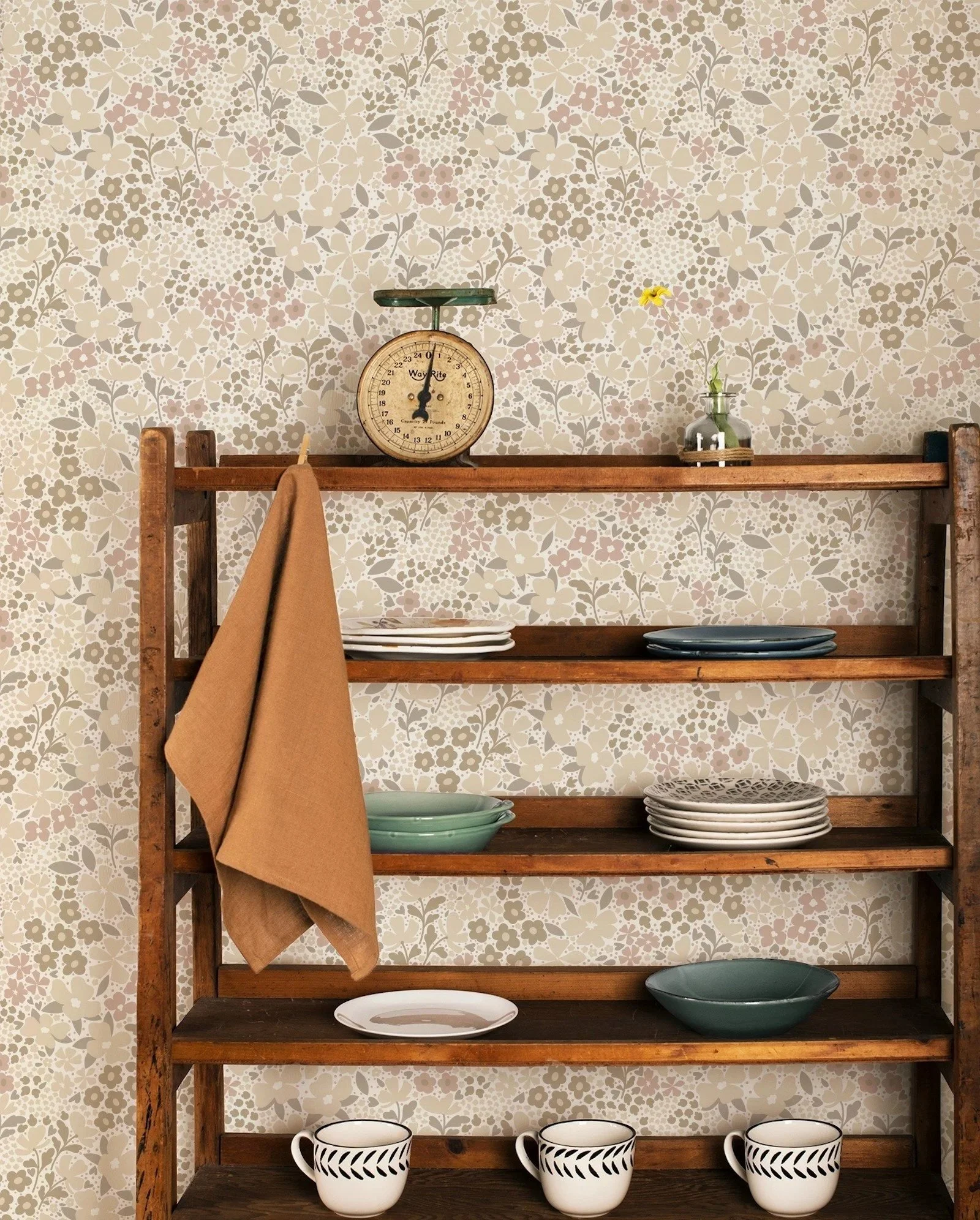 Wooden shelf with a vintage scale, a small vase with a yellow flower, various plates, bowls, and mugs against a floral wallpaper background.