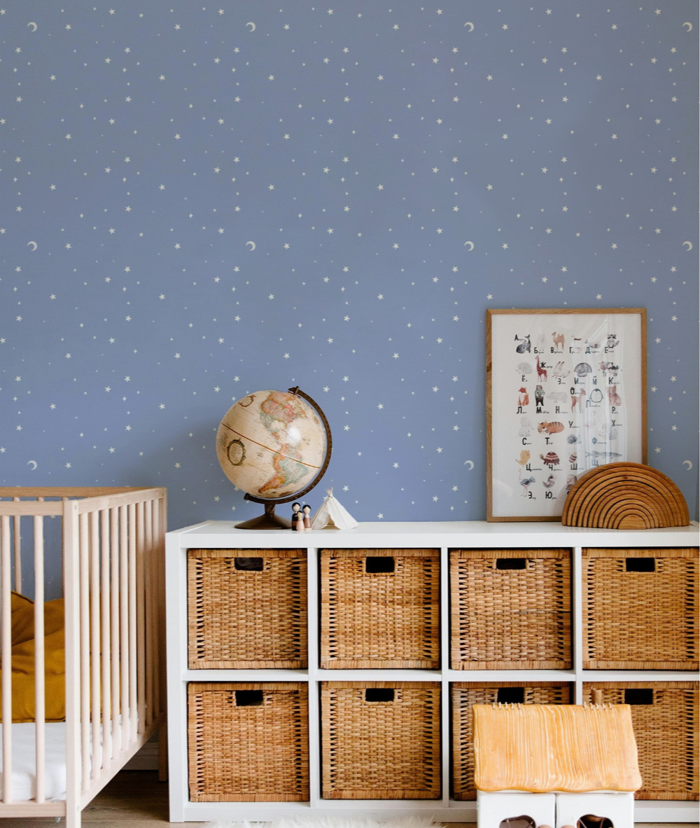 A nursery room with a blue wall decorated with stars and moon patterns, a white storage unit with woven baskets, a globe, framed art with alphabet animals, and various decorative items.