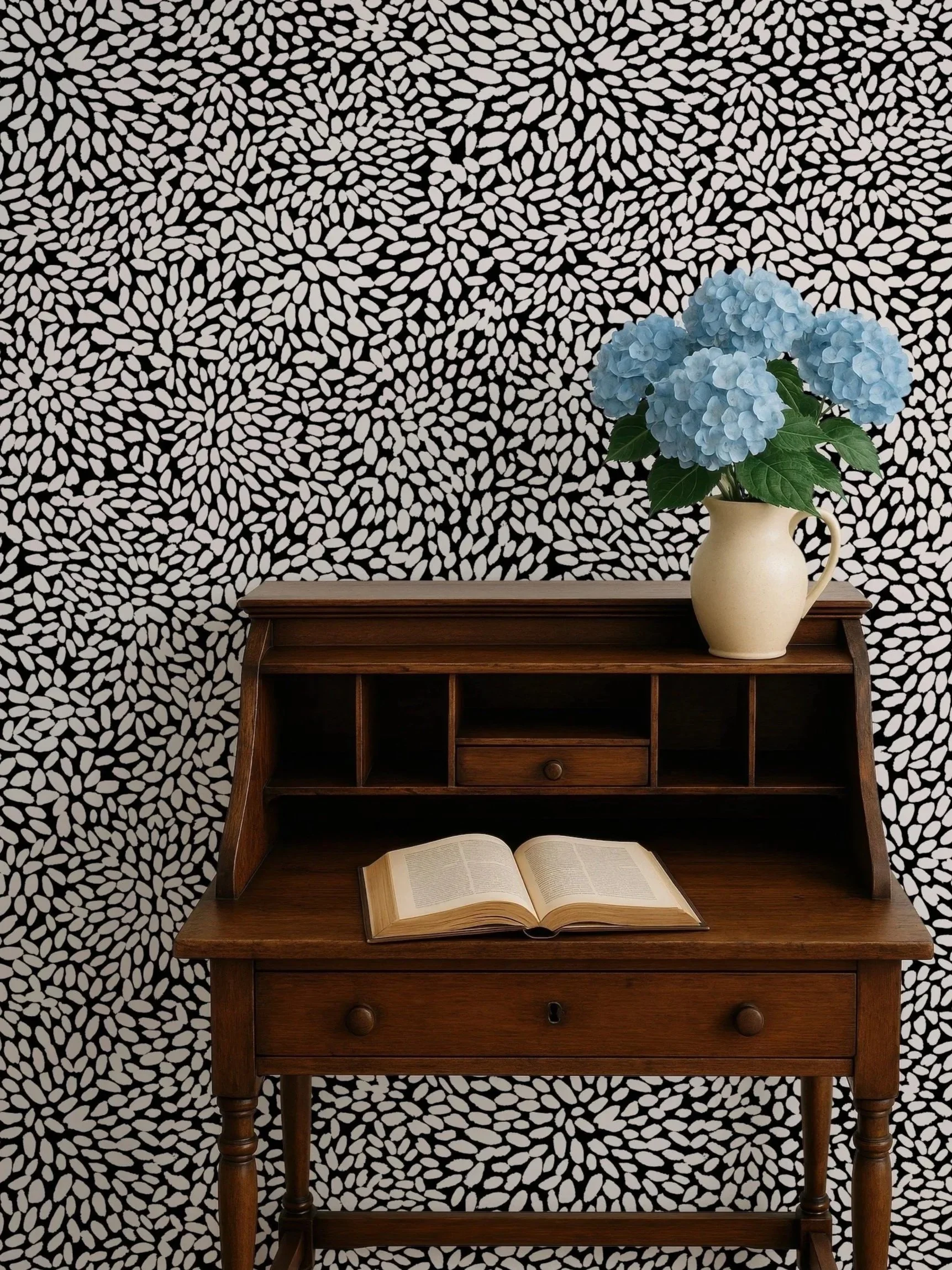 A wooden writing desk with shelves, an open book on its surface, and a beige vase with blue hydrangea flowers, set against a black and white patterned background.