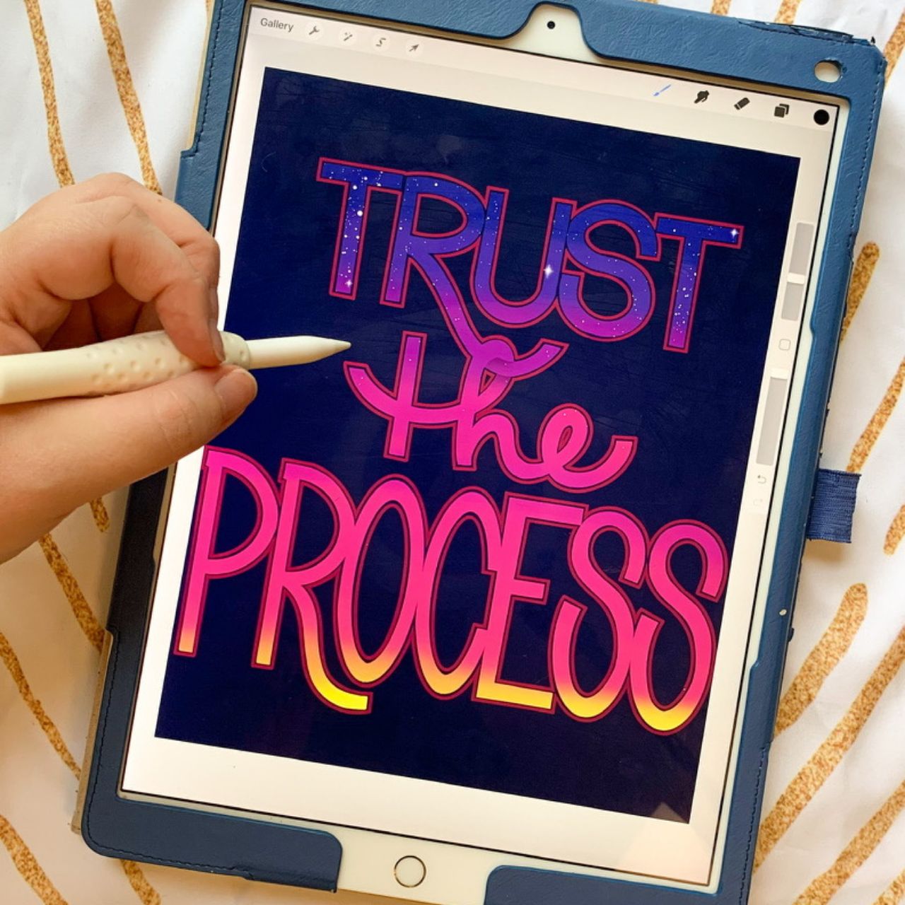 A digital tablet displaying the phrase 'Trust the Process' in colorful, neon-style text with a dark background. A person is holding a stylus and working on the text.