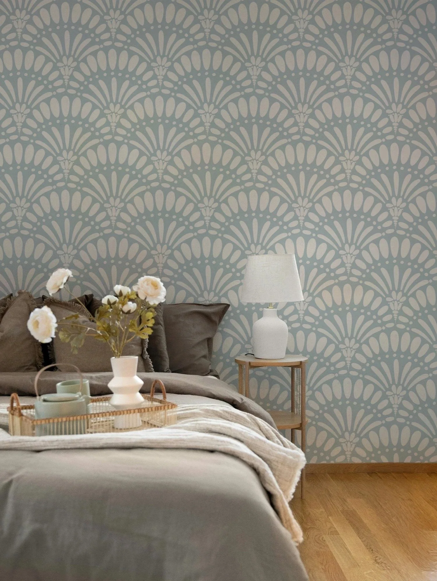 A cozy bedroom with a patterned wallpaper, a bed with brown pillows, a white vase with flowers, a tray with cups, and a bedside table with a white lamp.
