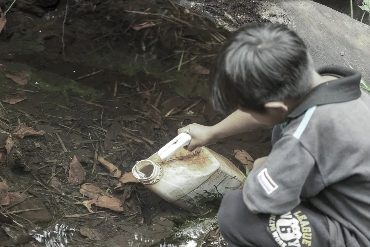 A child filling a container from a turbid spring