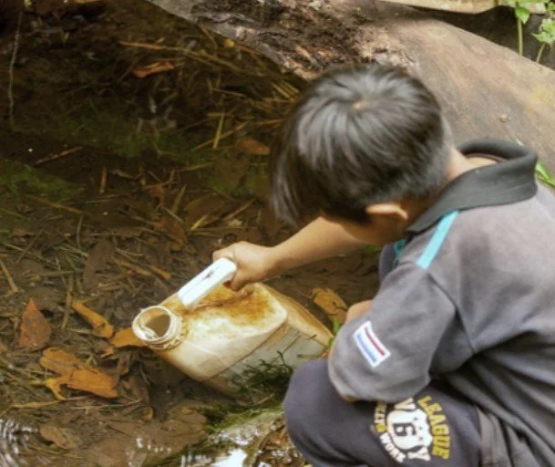 A child filling a container from a turbid spring