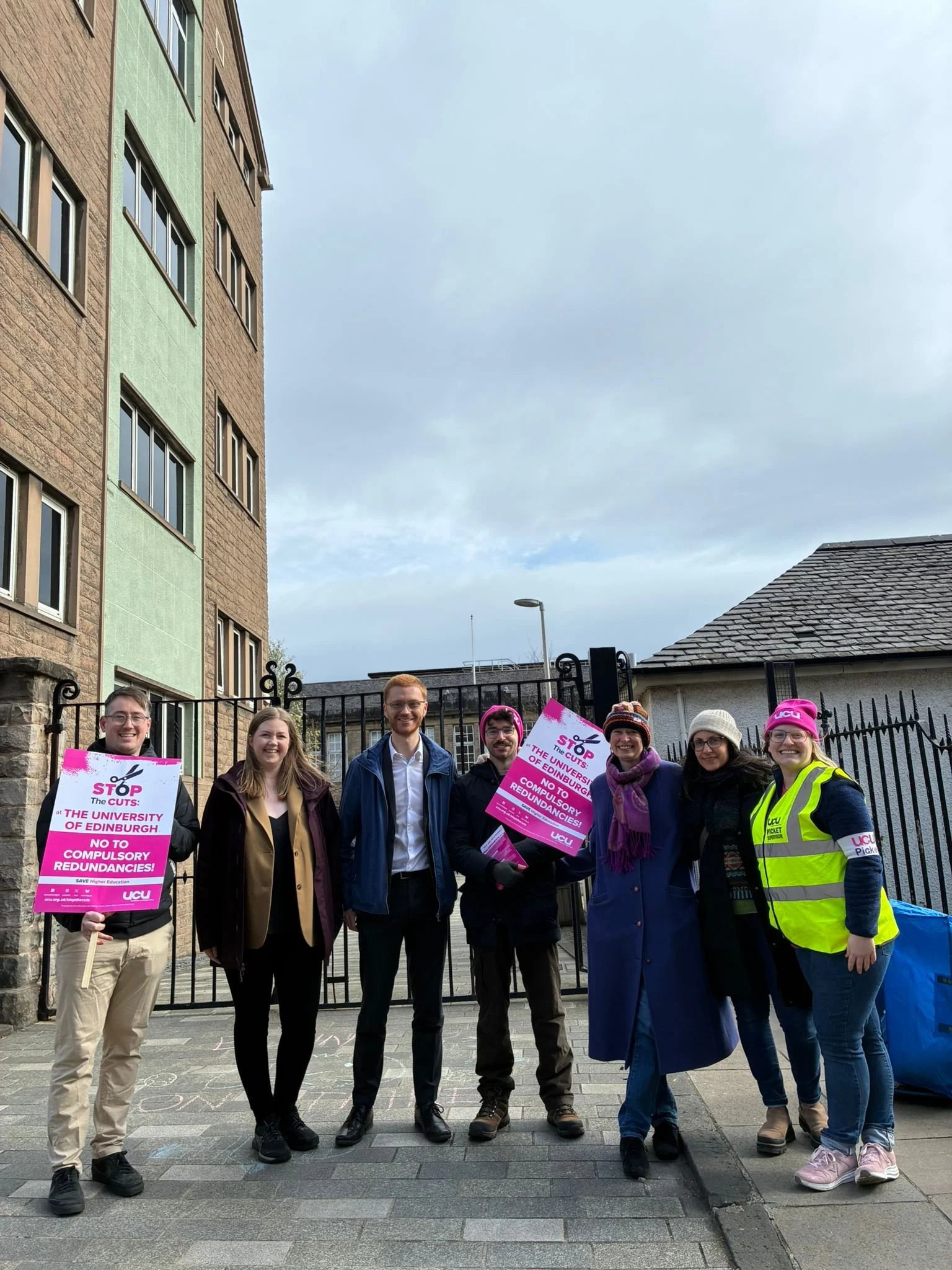 7 people standing side by side holding pink picket signs