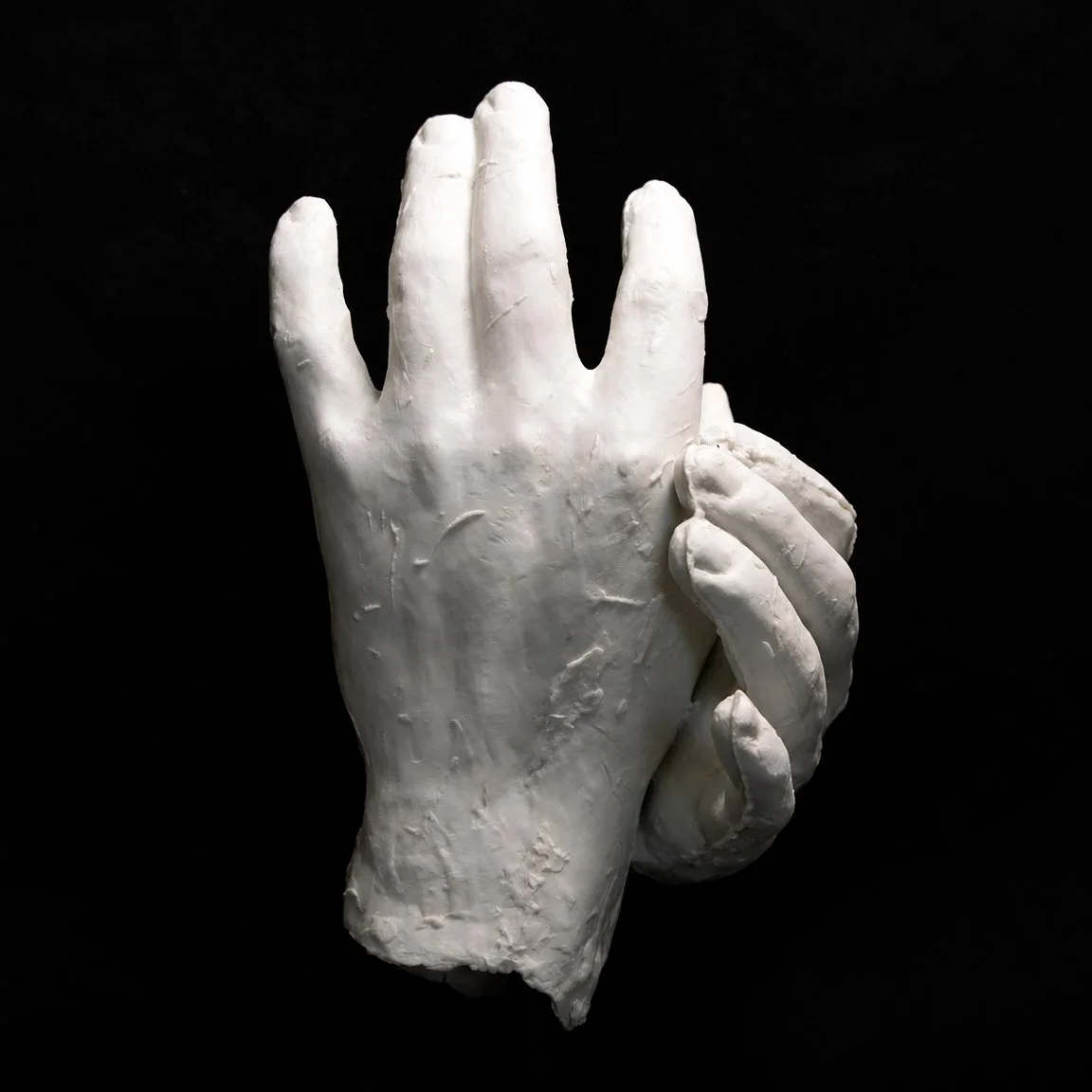 White sculpted hands touching, one palm facing outward while the other curls around it, against a black background.