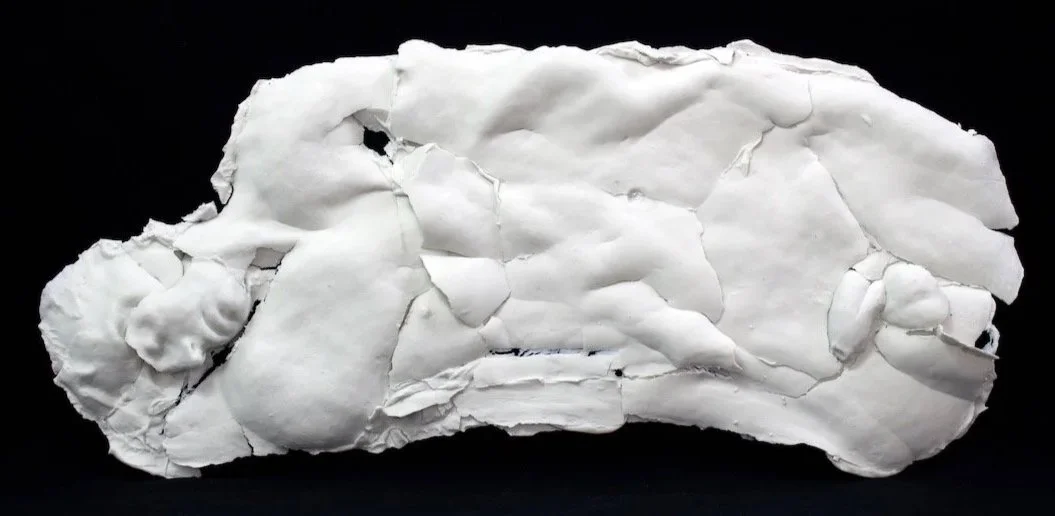 White fragmented porcelain reclining figure against a black background.