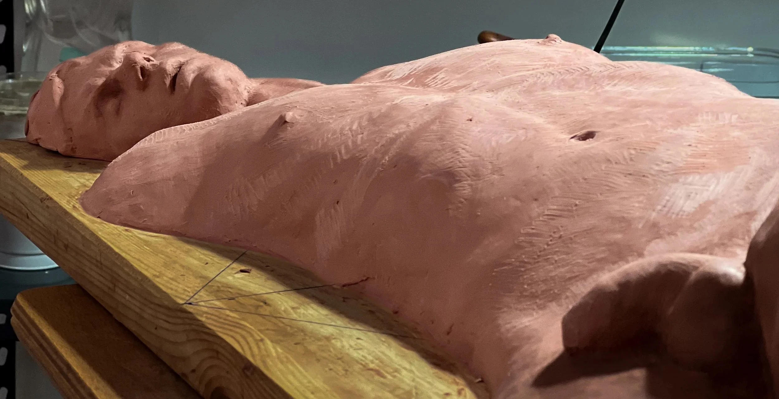 Reclining oil-based clay figure in progress on a wooden studio shelf.