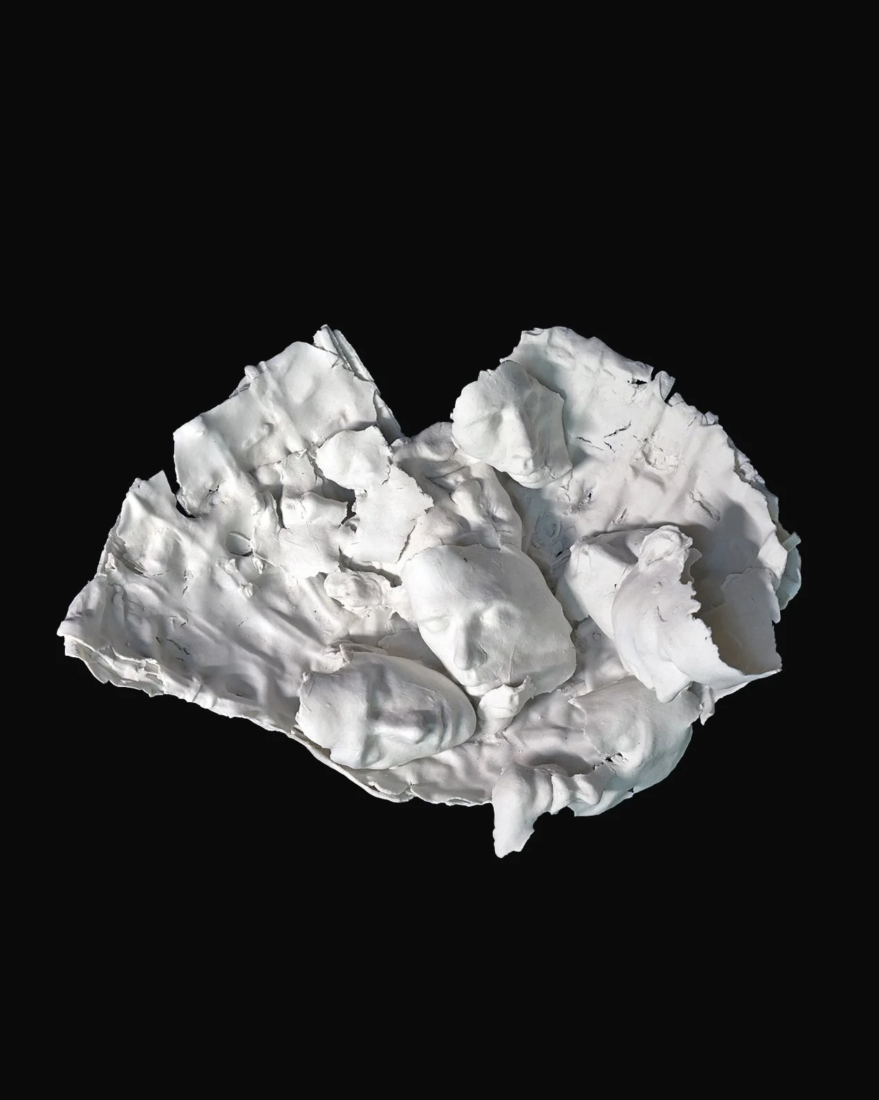 bisque porcelain sculpture composed of broken, folded porcelain sections with several partial faces lying on the surface. the piece reads as an accumulation of fragments, cracks, and impressions, photographed on black.