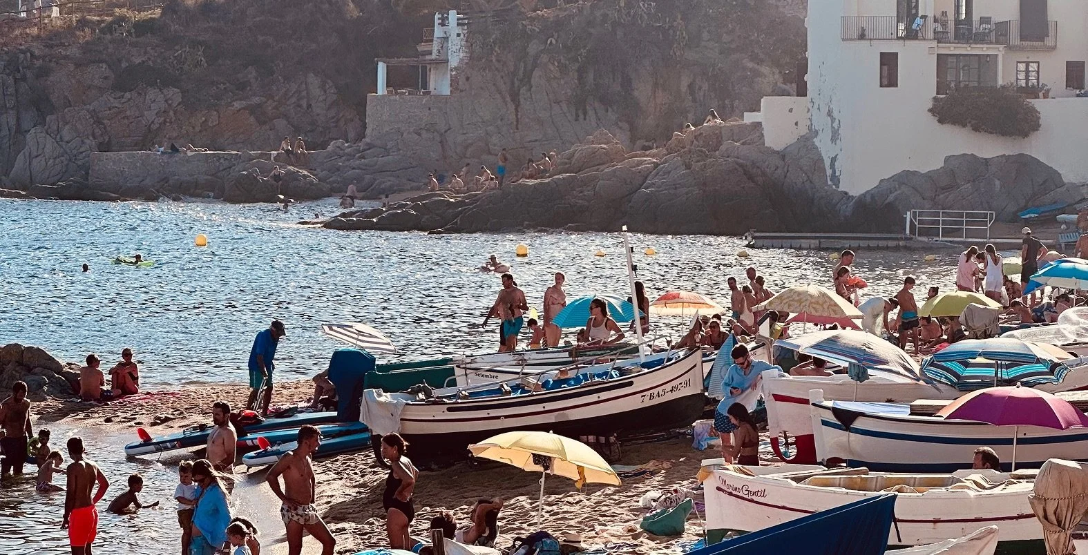 Busy fishing village beach with traditional boats and sunbathers on the Costa Brava