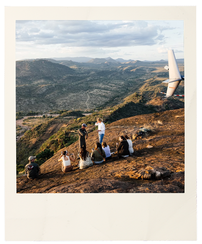 Group of travellers sitting on a rocky hilltop overlooking an African landscape at golden hour