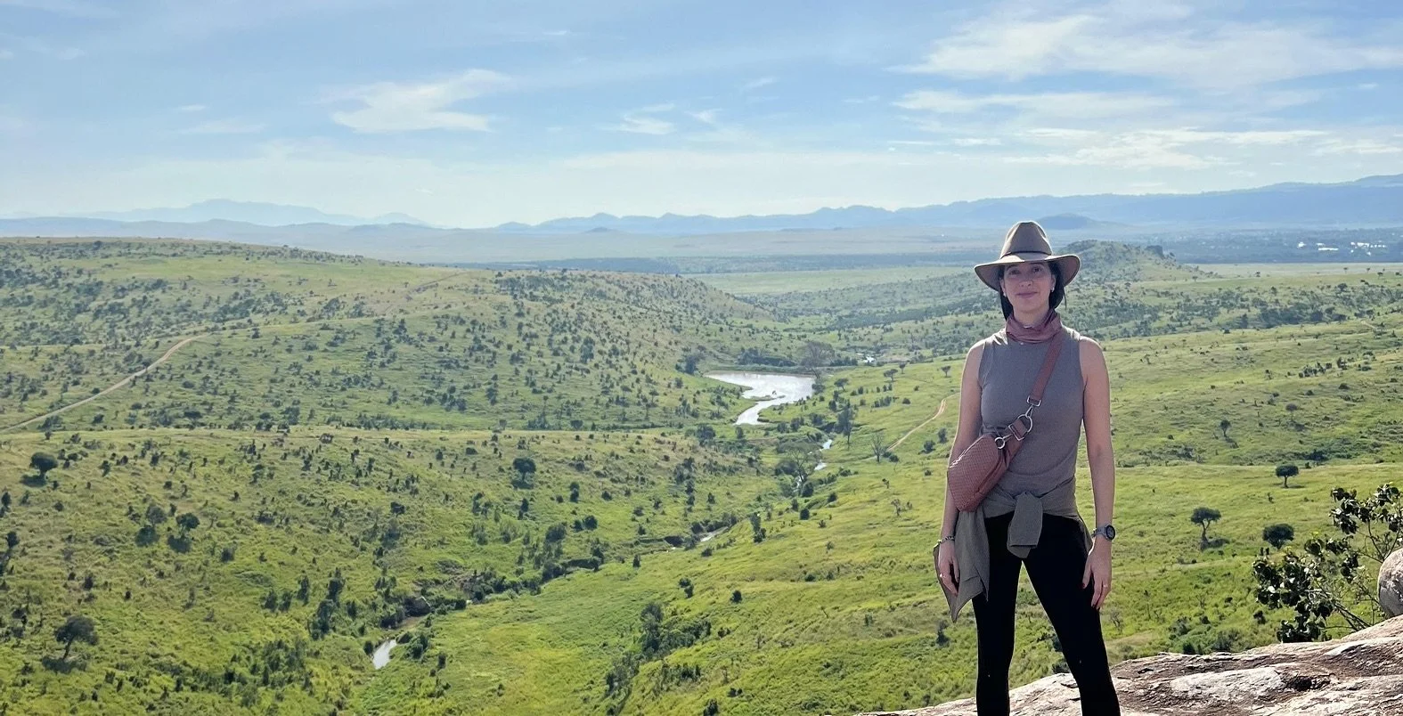 Woman standing on a rocky outcrop overlooking a vast green African valley and winding river