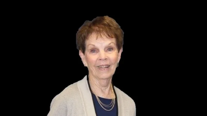 Elderly woman with short hair smiling against a black background.