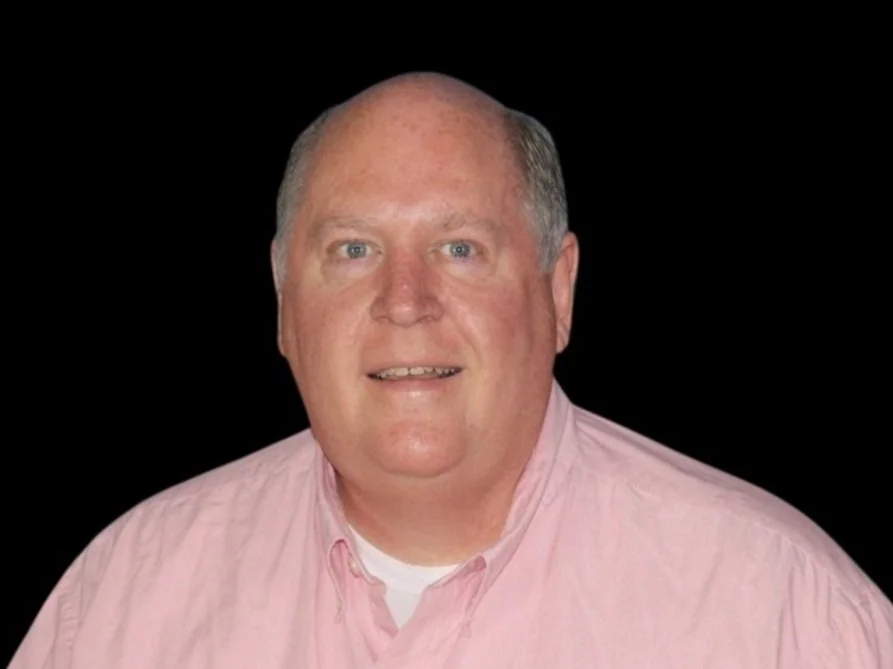 A person wearing a pink shirt against a black background.
