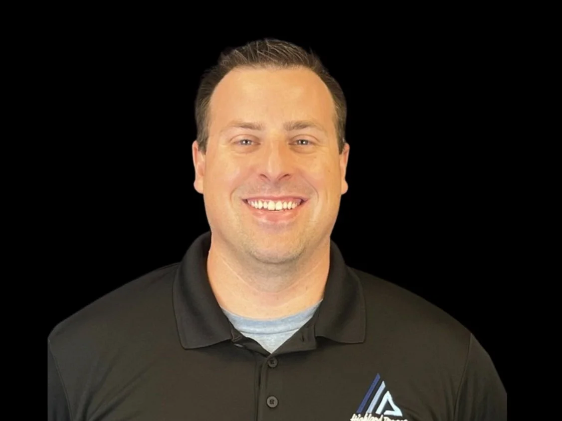 Smiling man in black polo shirt with company logo, black background.