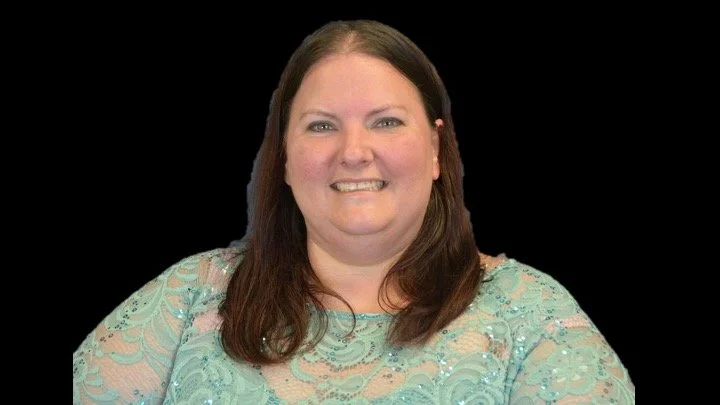Smiling person in a blue lace top on a black background.