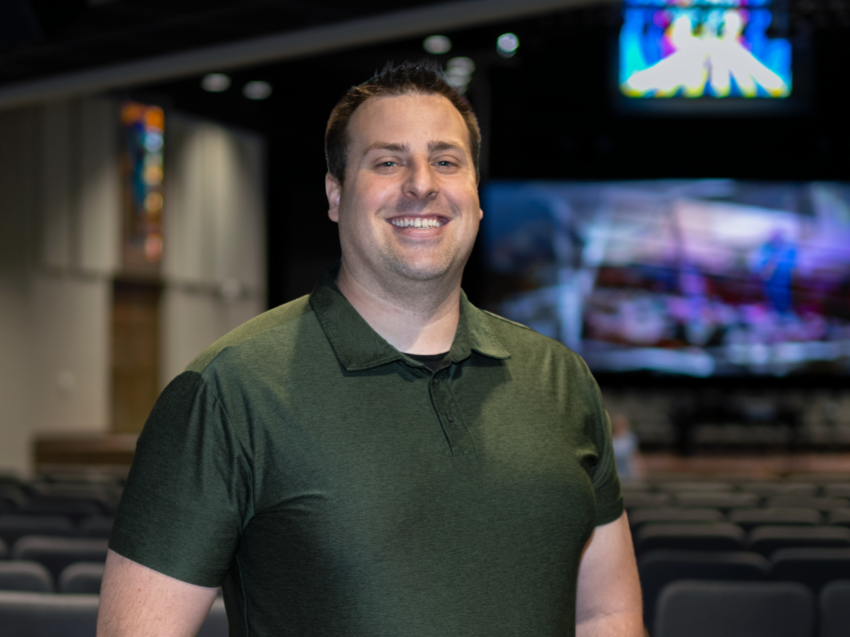 Smiling man in black polo shirt with company logo, black background.