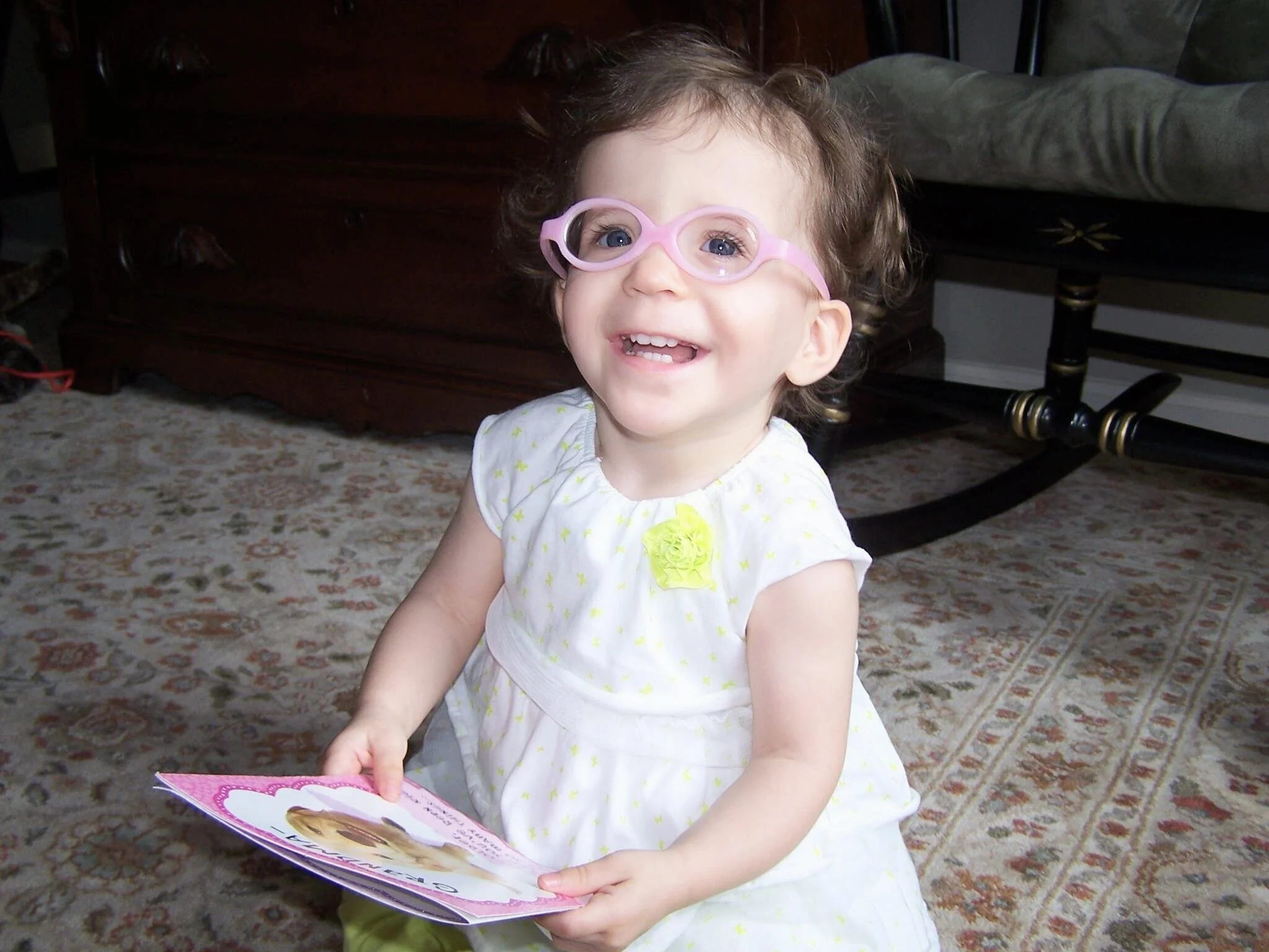 1 year old little girl smiling at camera holding a book