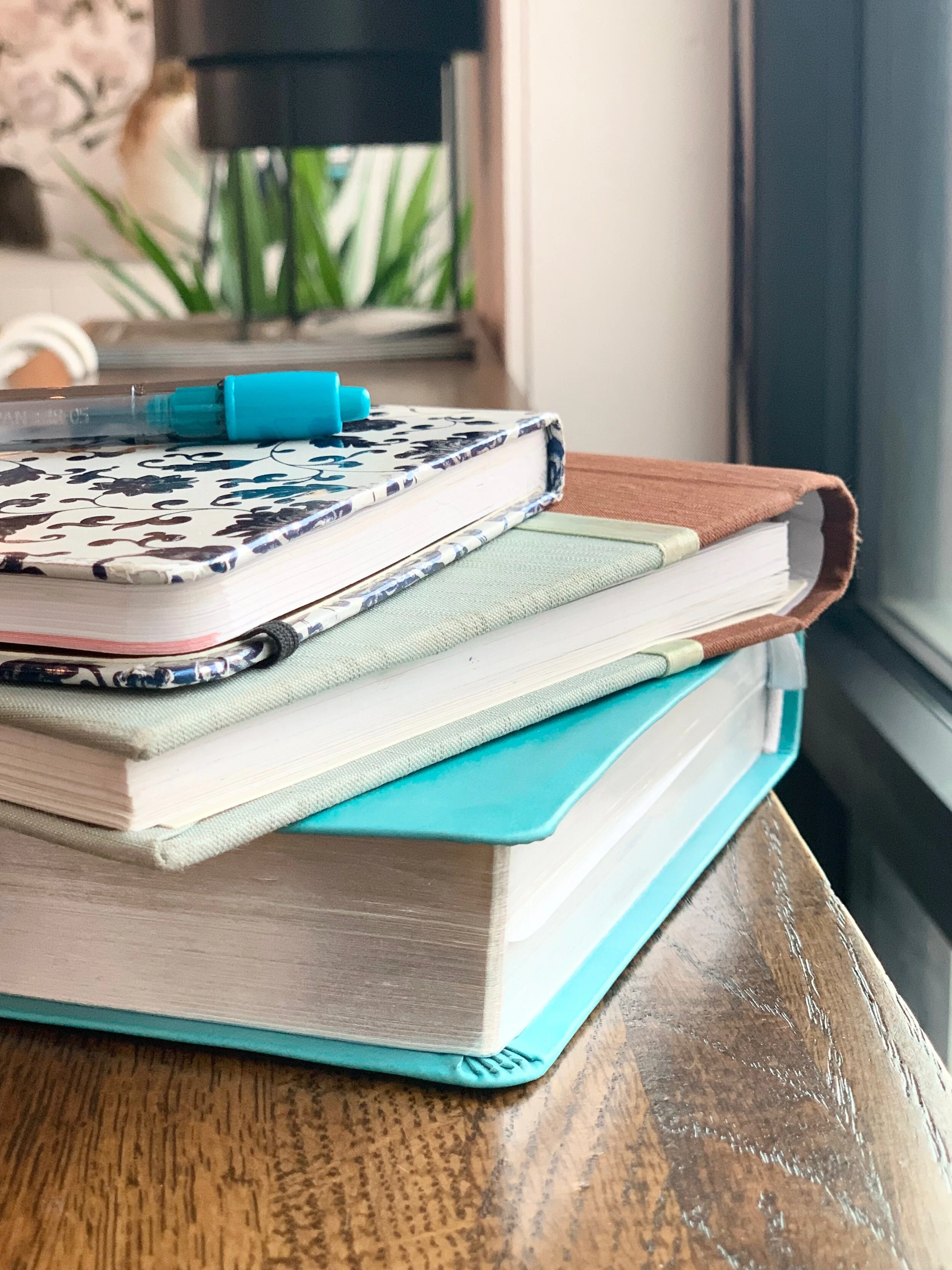 Colorful blue writing journals stacked up with a blue pen on the top of the stack