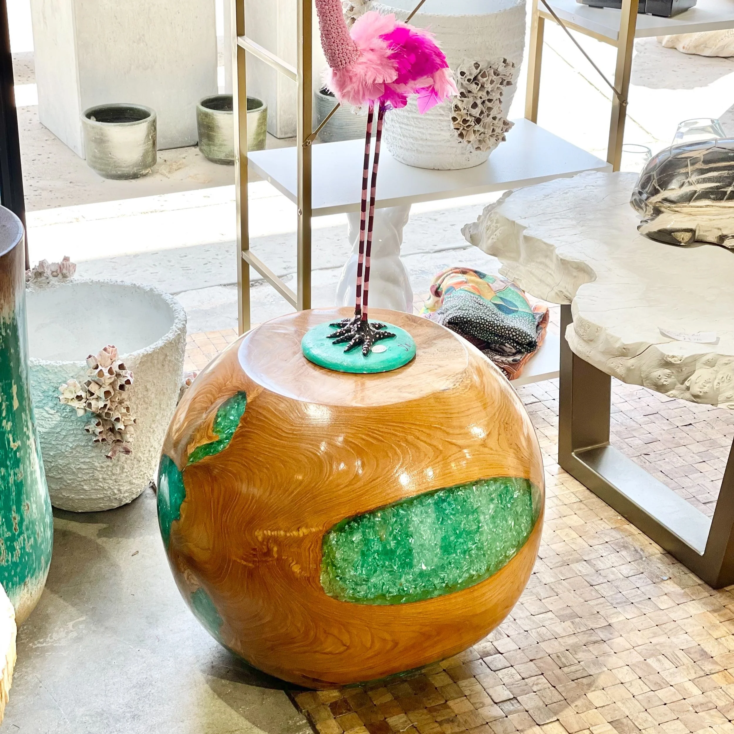 Decorative art piece resembling an orange with green details, topped with a pink fluffy unicorn and a black and white striped leg, situated among other decorative items and pottery.