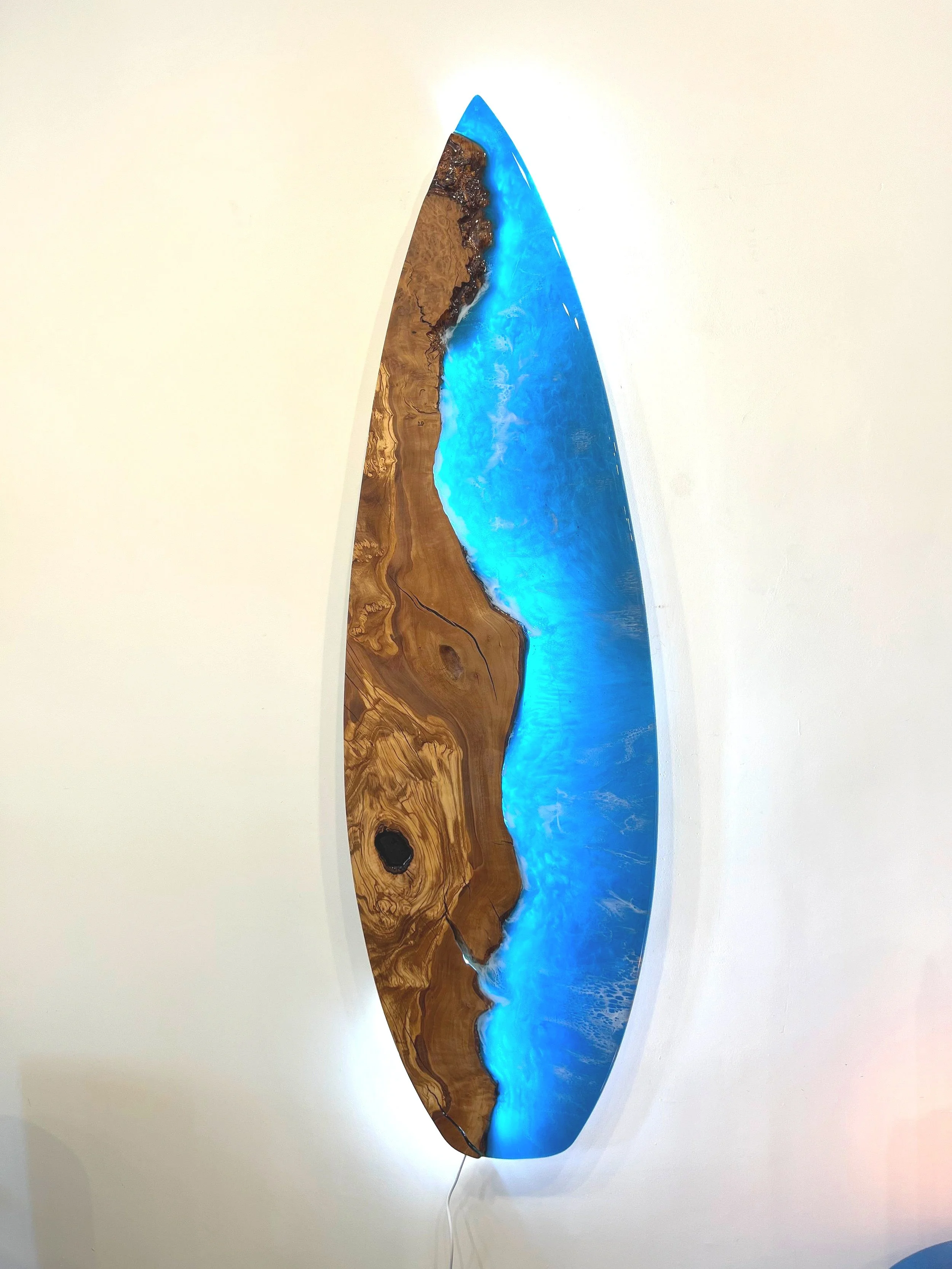 Epoxy resin surfboard-style art piece with natural wood and blue resin sections against white wall
