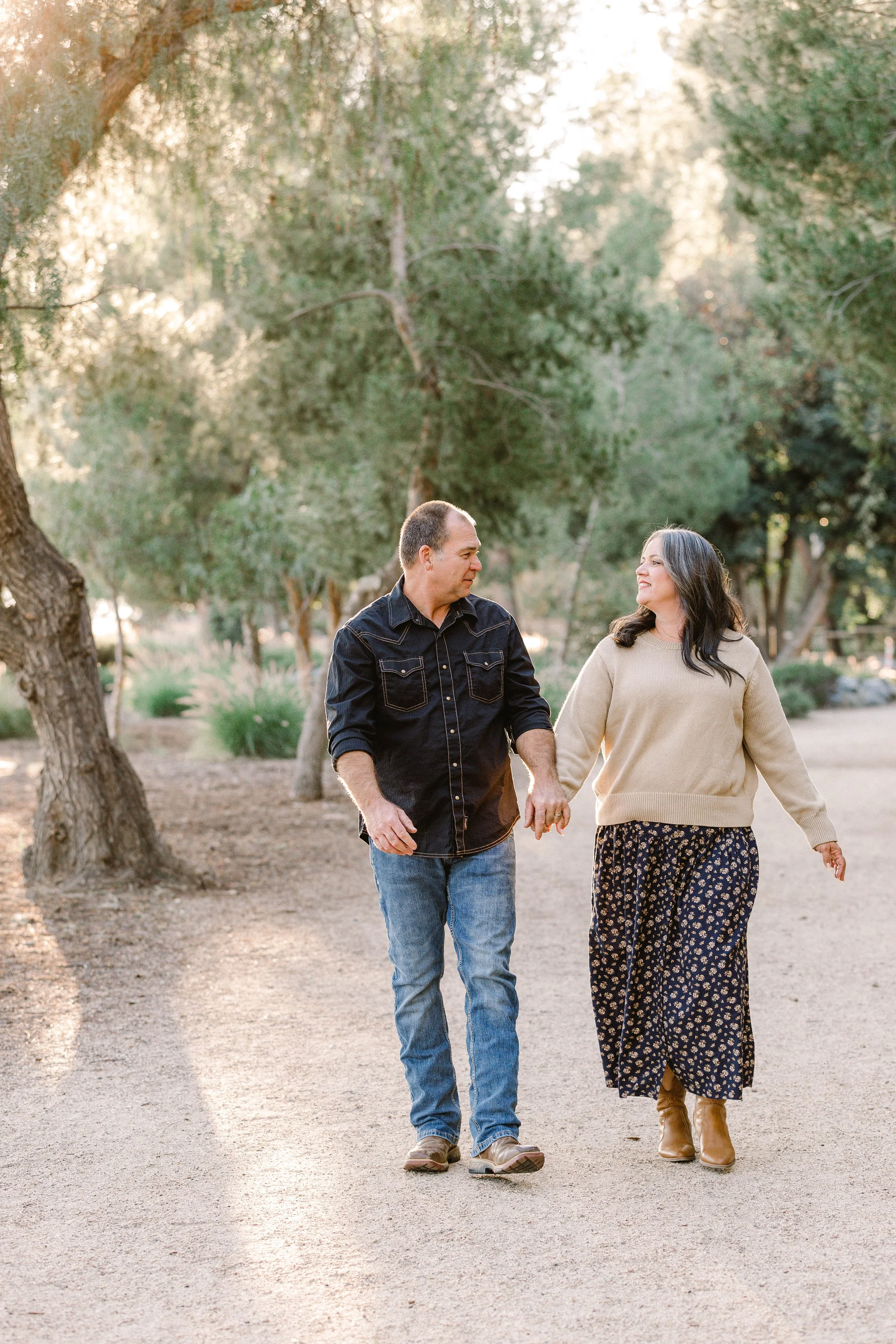 Couple walks hand in hand down dirt path surrounded by green trees