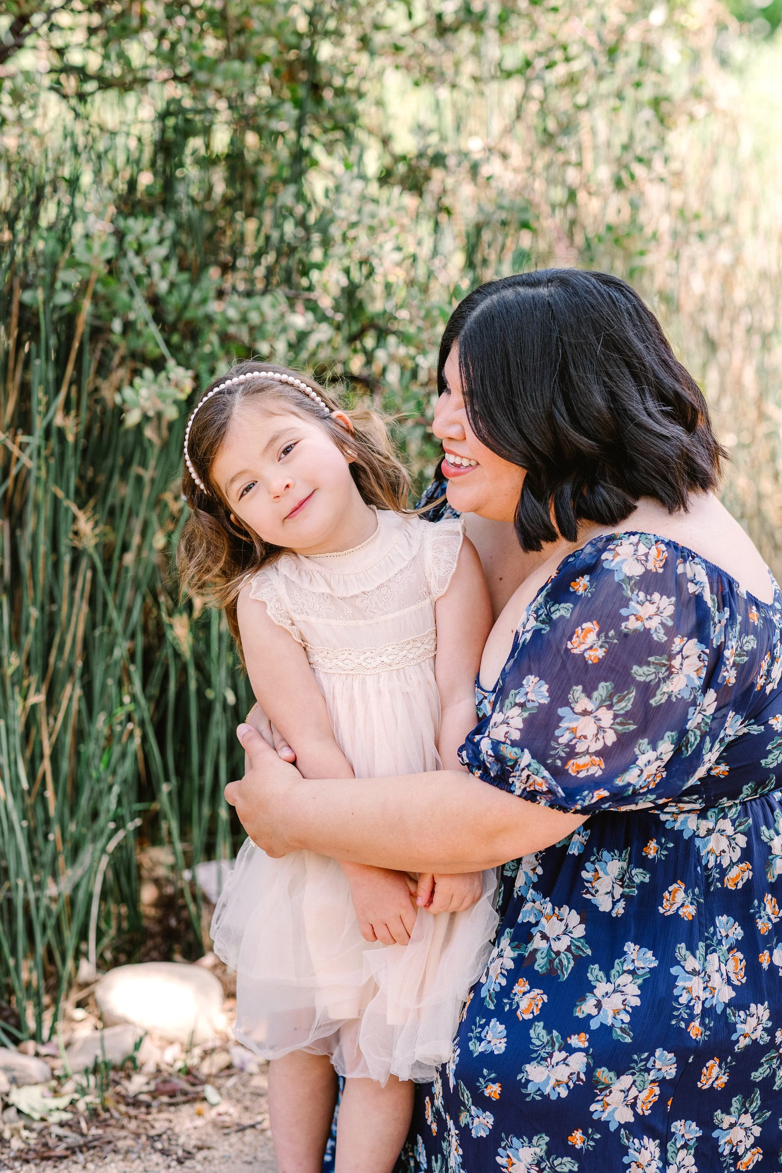 A woman hugging a young girl in a park with tall plants in the background