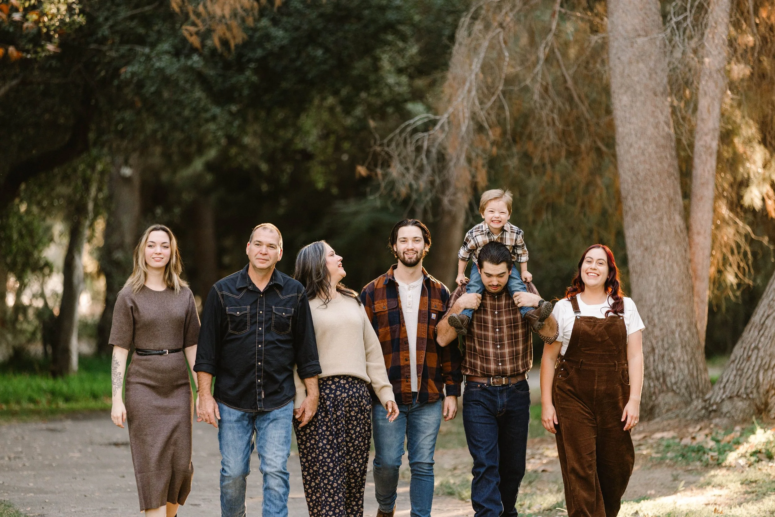 group of seven people walking outdoors in a park, smiling and enjoying each other's company, with large trees in the background