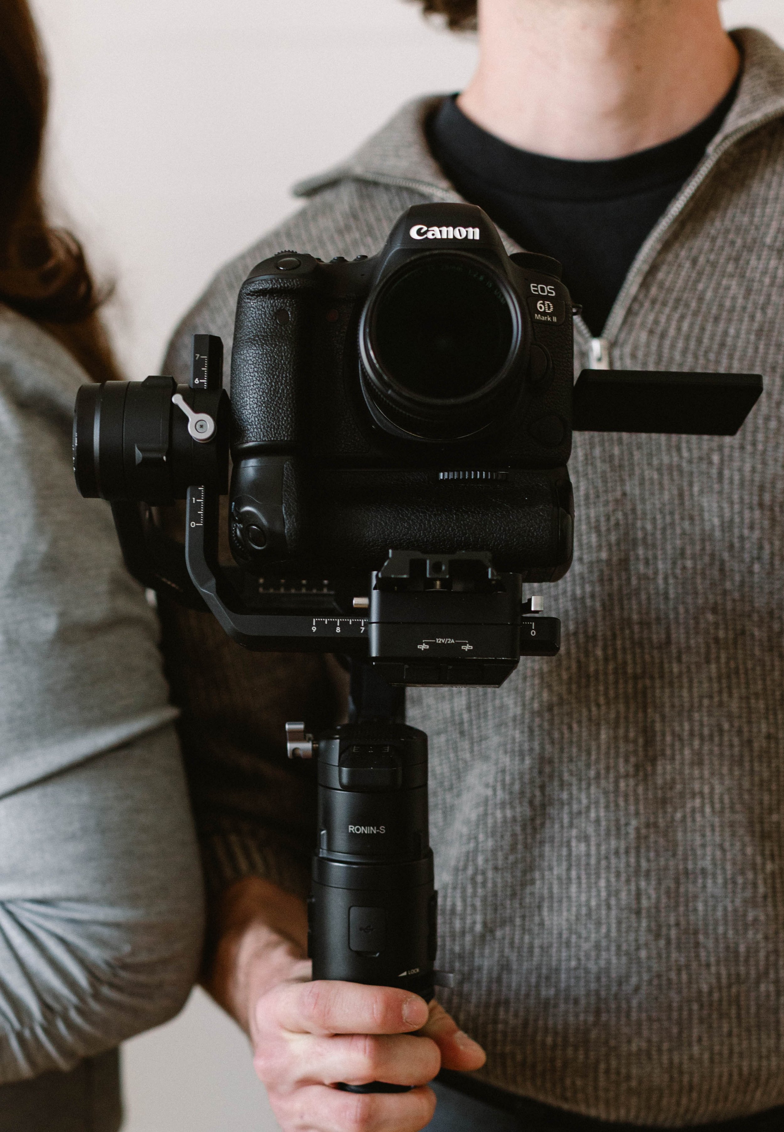 Close-up of a person holding a camera stabilized on a gimbal, with another person partially visible beside them.